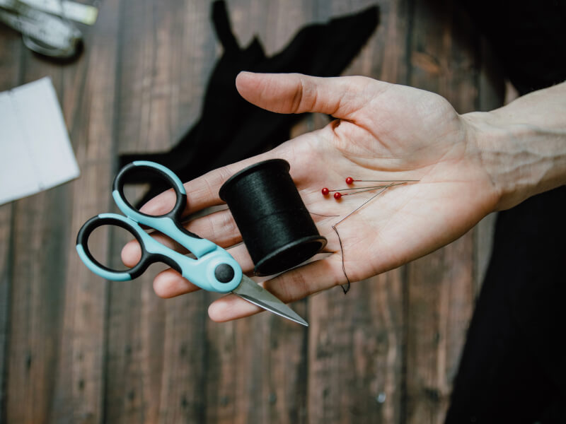 A person holding sewing scissors, thread and pins in their hand.